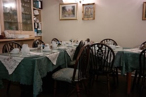 A dining area with tables set for four, wooden chairs, and a cabinet with glass doors. - Acorn Guest House (Cambridge)
