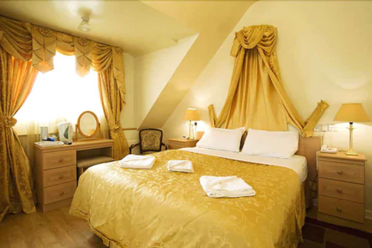 A hotel room with a large bed, a desk, a chair, and two bedside tables with lamps.