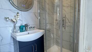 Une salle de bain avec une douche à l’italienne, un lavabo blanc et un meuble sombre, ainsi qu’un miroir rond accroché au mur.