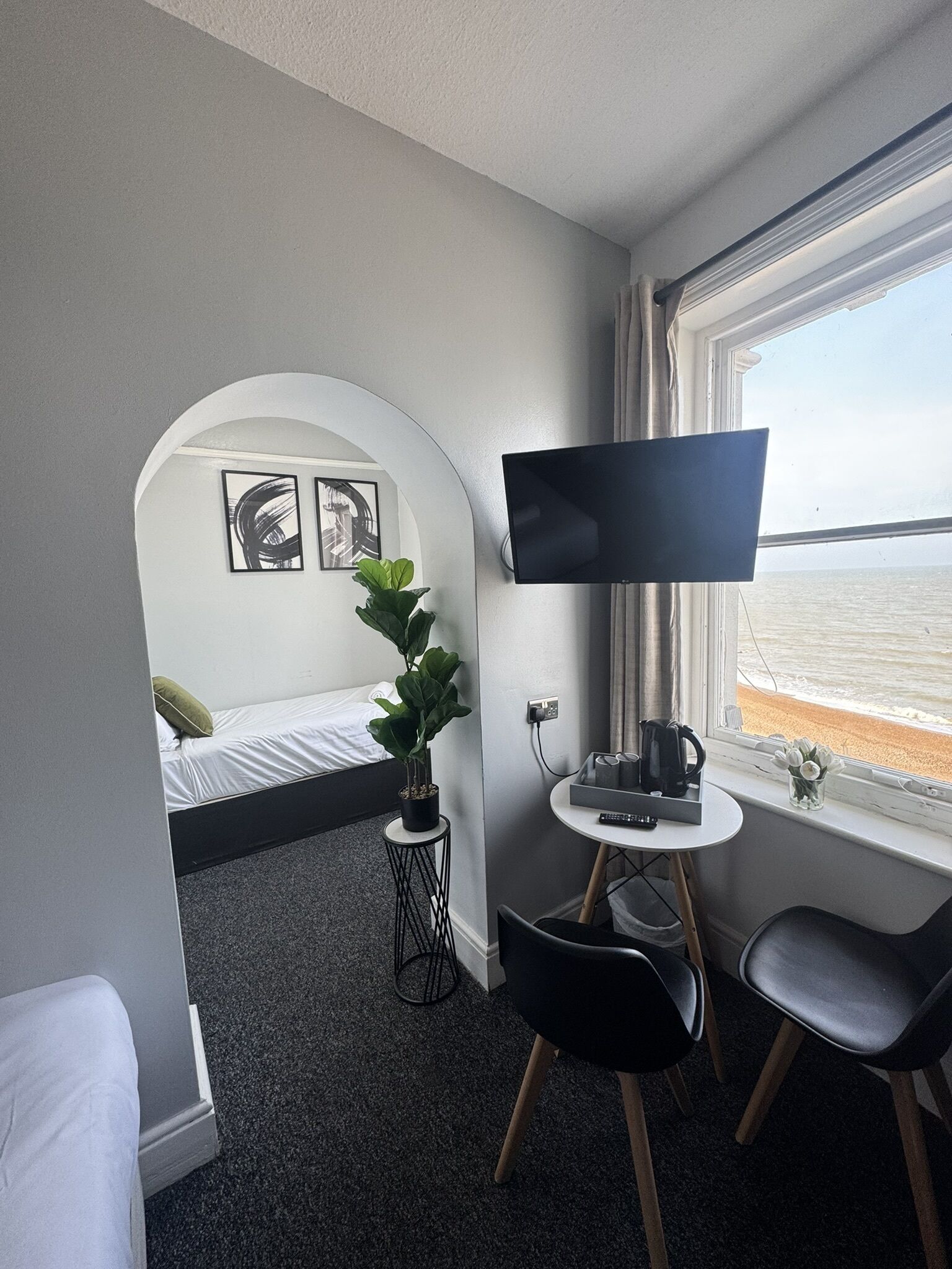 Ein Zimmer mit Bett, Fernseher, Schreibtisch und Fenster mit Meerblick.