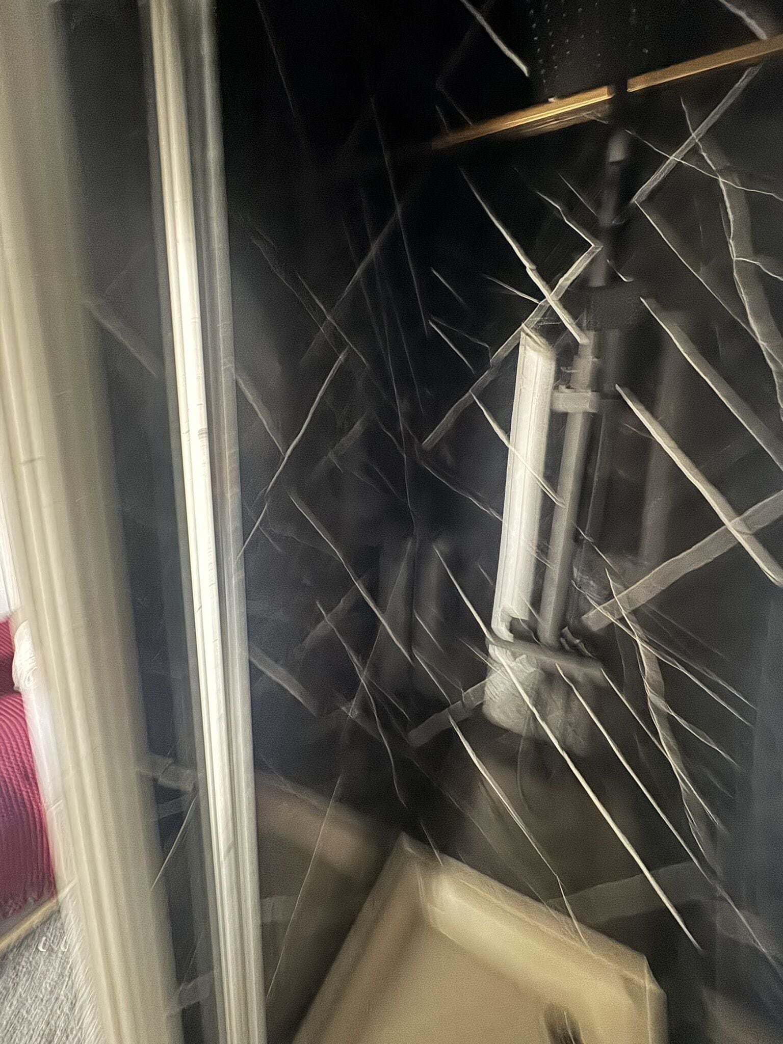 Een badkamer met een douchecabine van glas, een wit wastafeltje en een zwart betegelde muur.