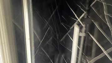 Een badkamer met een douchecabine van glas, een wit wastafeltje en een zwart betegelde muur.