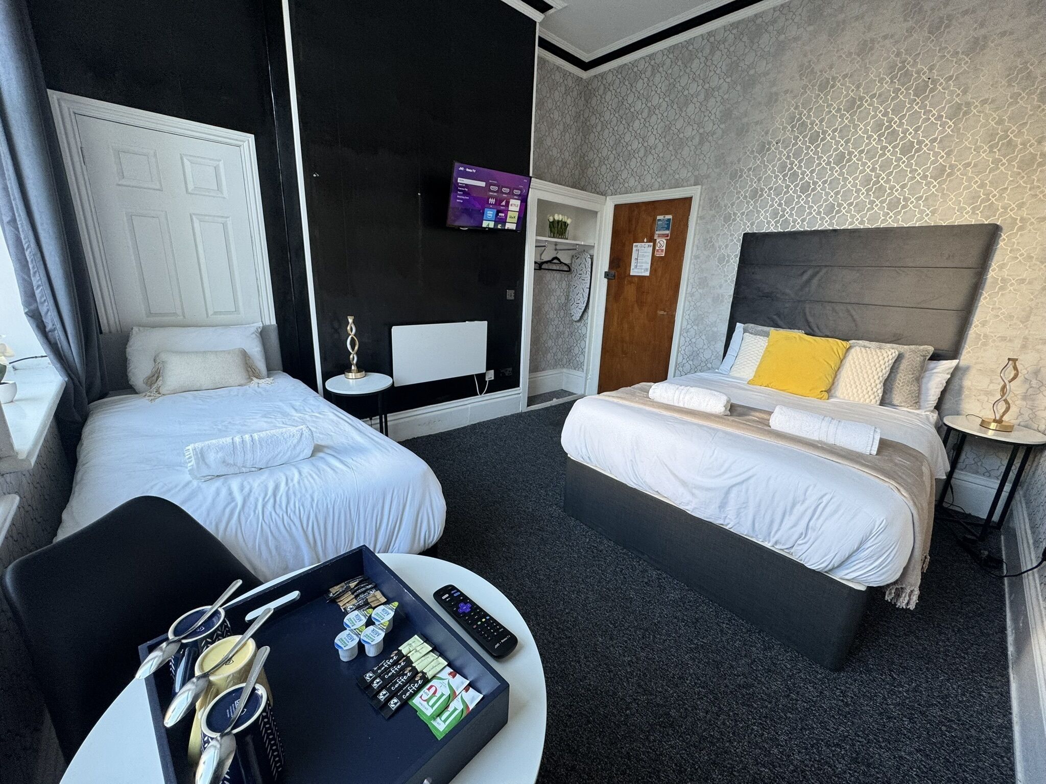 A hotel room with two beds, a desk with breakfast items, a TV, and a coat rack.