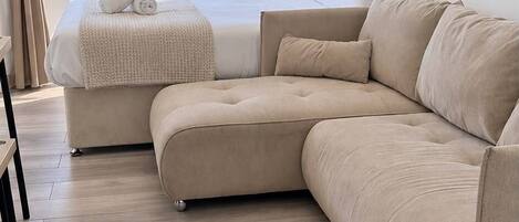 A modern living room with a beige sectional sofa, a small ottoman, and a view of the ocean through large windows.