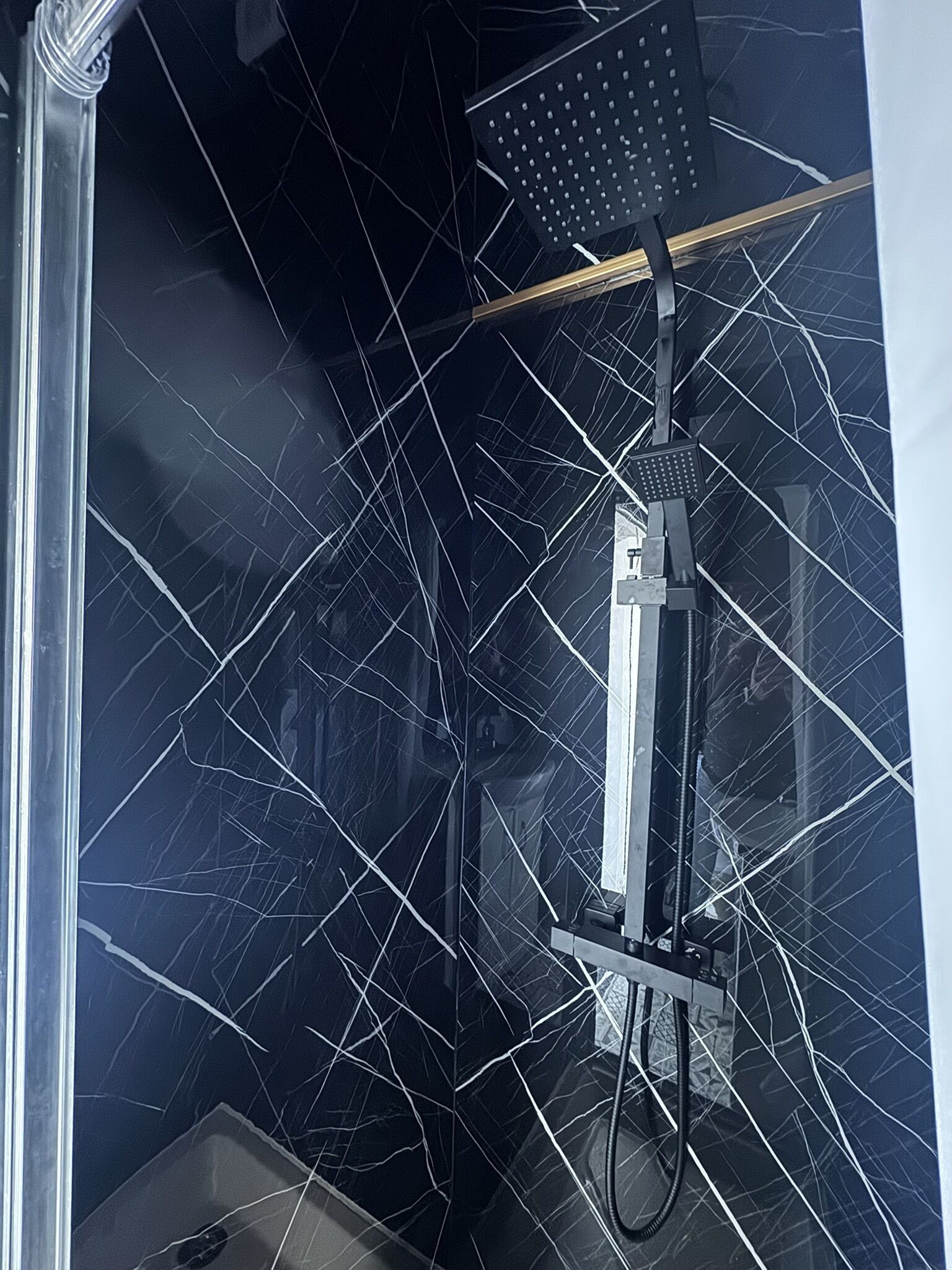 A shower with a cracked glass wall and a handheld showerhead.