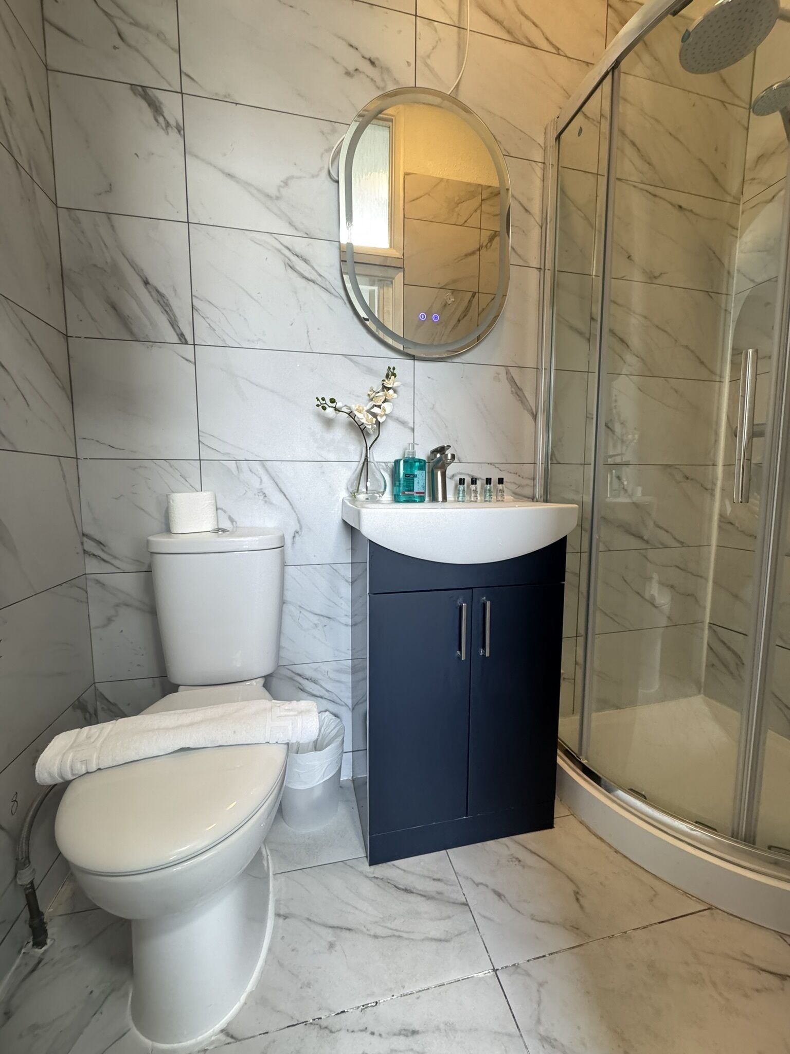 Een badkamer met toilet, wastafel voorzien van toiletartikelen, een spiegel en een douche.