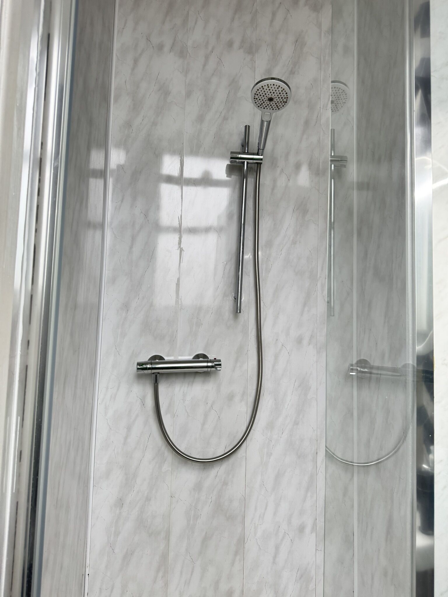 A shower with a handheld showerhead and a wall-mounted control.