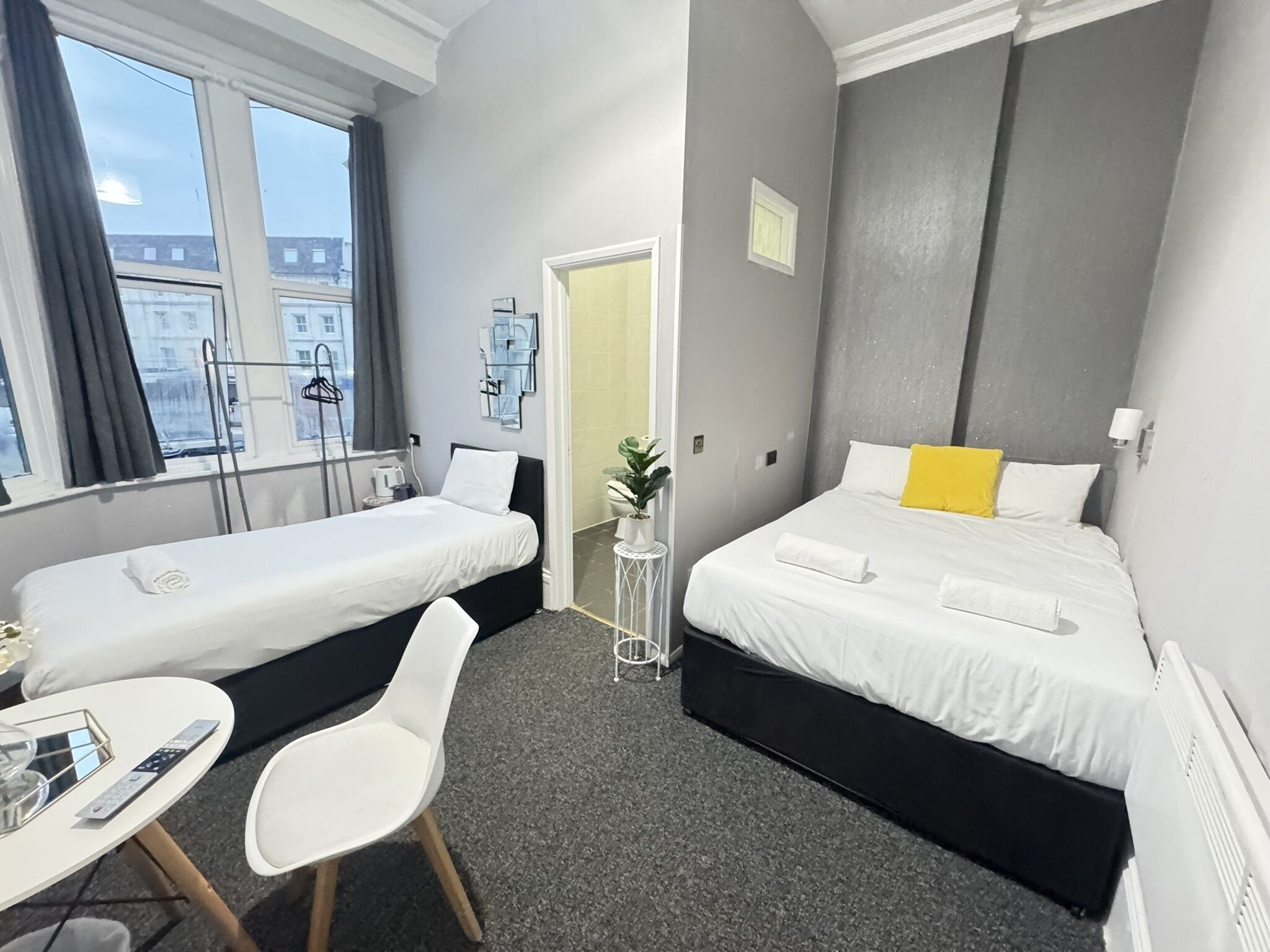 Une chambre d’hôtel avec deux lits, une petite table, une chaise et une fenêtre avec des rideaux.