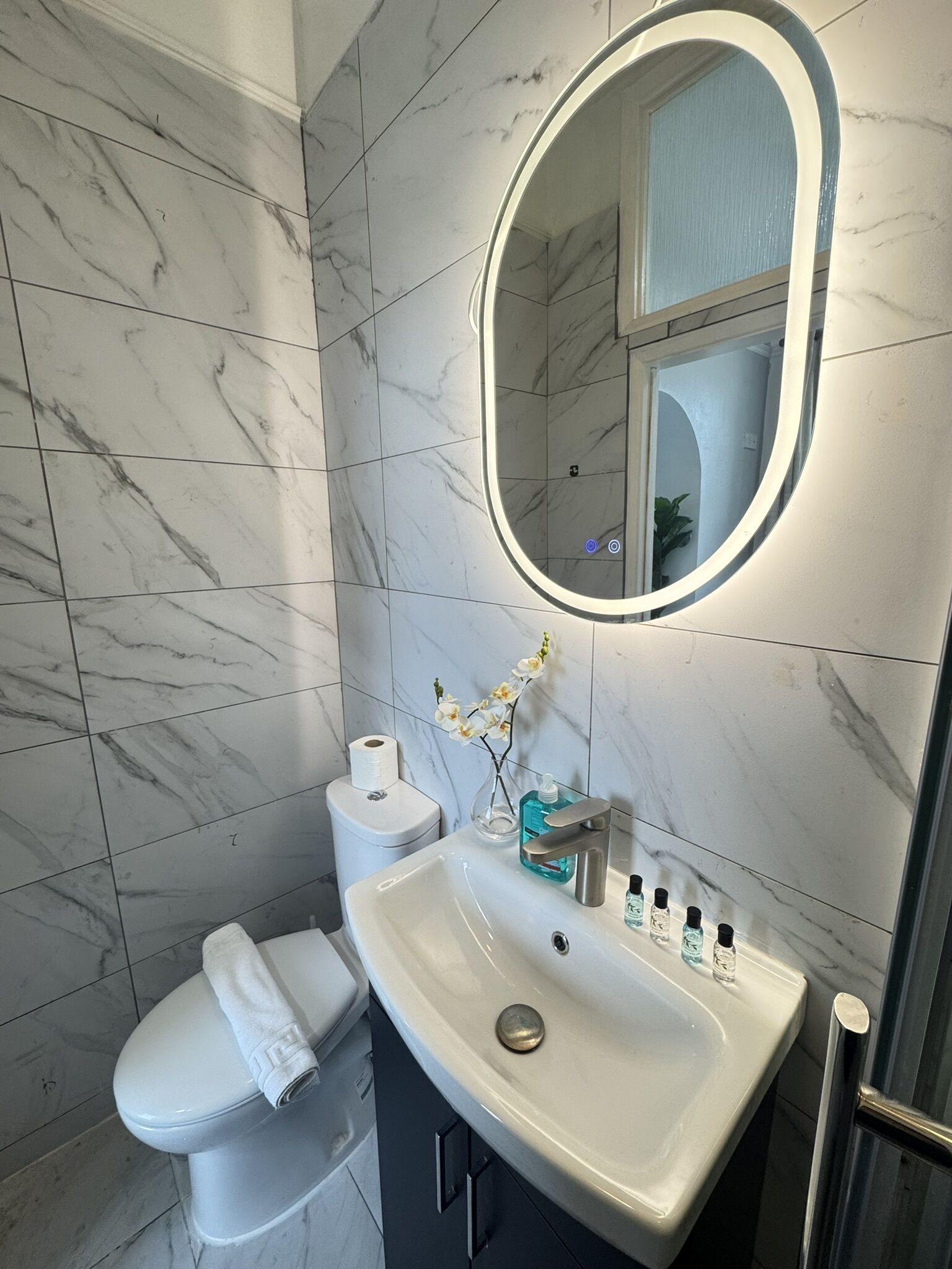 Un baño con inodoro blanco, lavabo con espejo y zona de ducha.