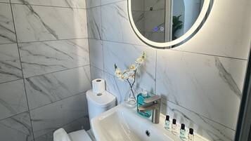 Un baño con inodoro blanco, lavabo con espejo y zona de ducha.