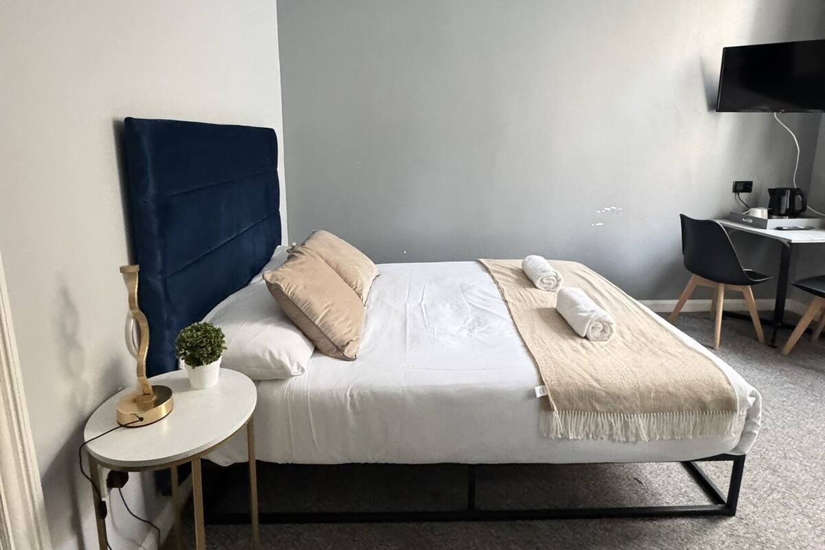 A neatly arranged hotel room with a bed, bedside table, lamp, and a desk with a chair.
