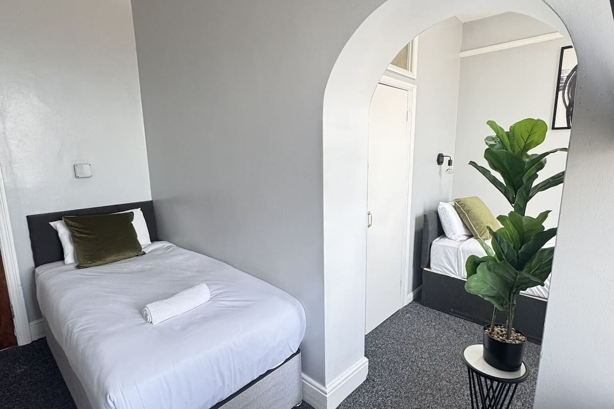 A hotel room with a bed, a desk, a chair, a potted plant, and a mirror.
