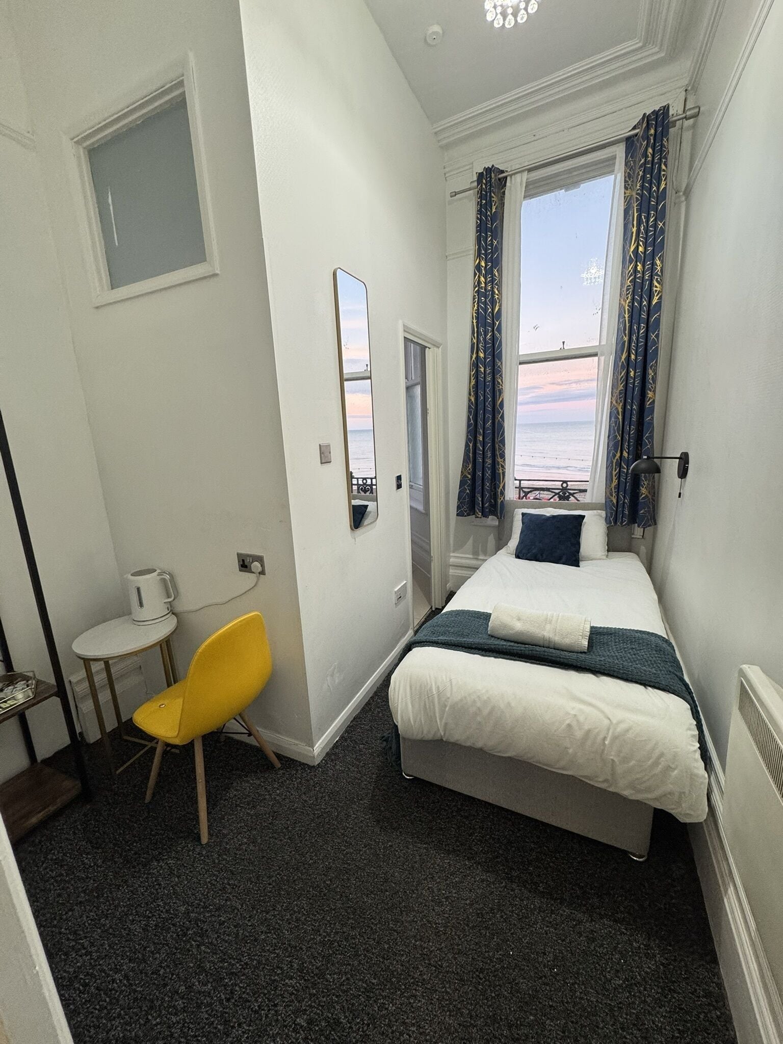 Una habitación de hotel con cama, una silla, una mesita y un ventanal con cortinas.