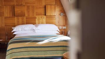 A bedroom with a wooden headboard, a bed with white bedding, and a bedside table with a lamp.