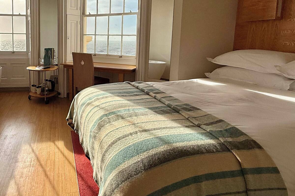 A hotel room with a large bed, a desk, and a window with a view of the sea.