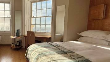 A hotel room with a large bed, a desk, and a window with a view of the sea.