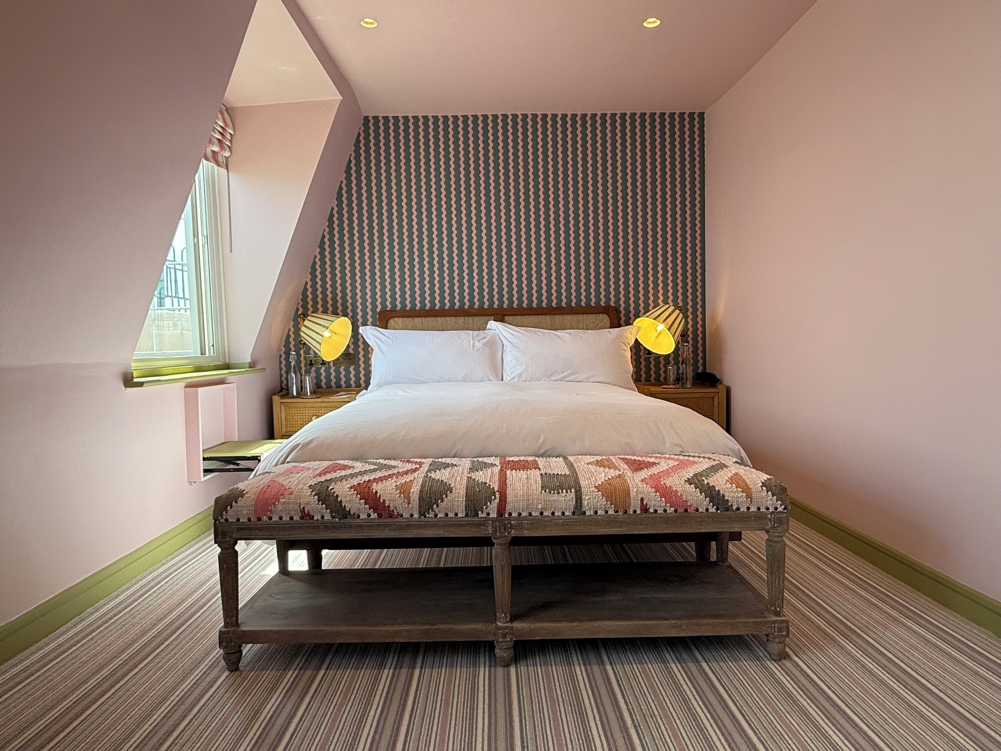 Ein Schlafzimmer mit einem Bett, Nachttischlampen, einem Fenster und einem gemusterten Teppich.