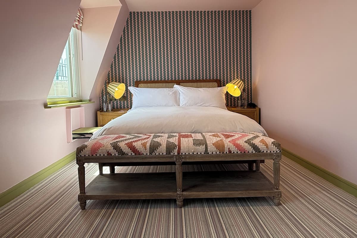 A bedroom with a bed, bedside lamps, a window, and a patterned carpet.