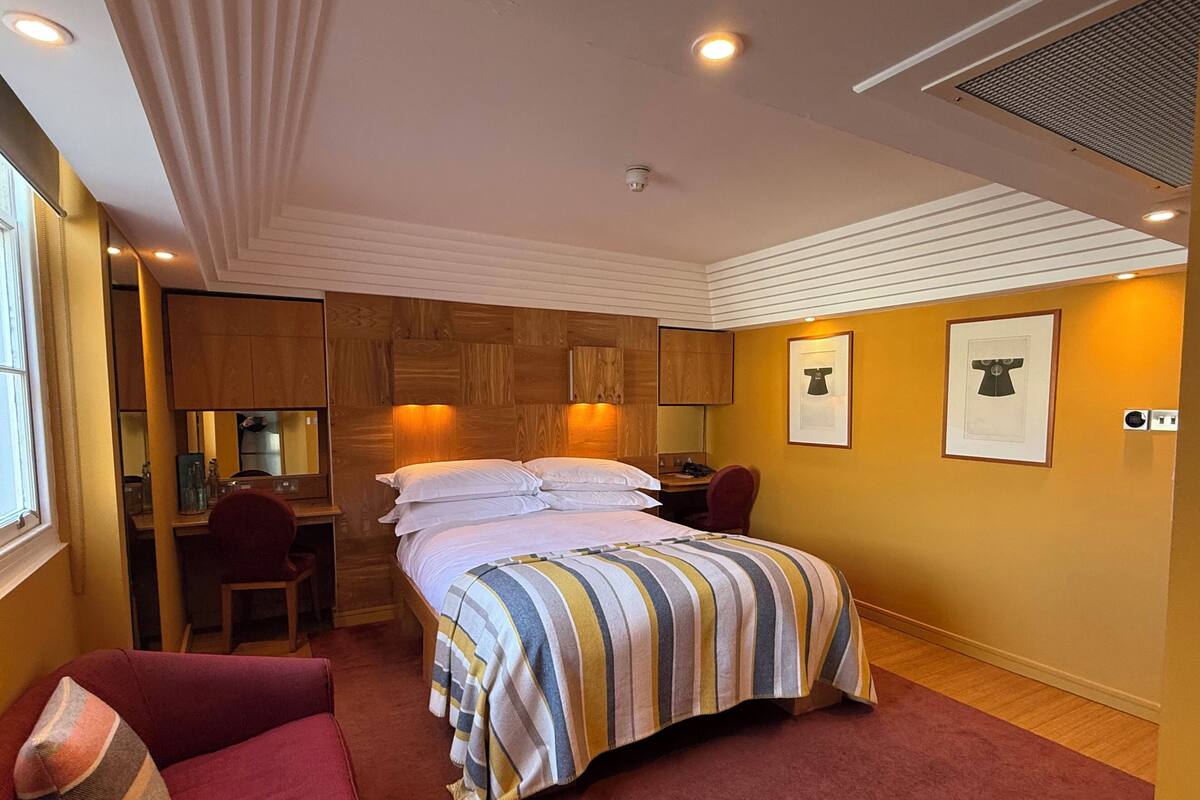 A hotel room with a bed, a desk, a chair, and a small kitchenette.