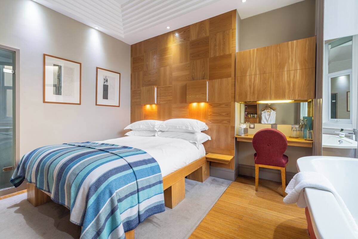 A modern bedroom with a bed, bedside table, chair, and a bathroom with a sink and mirror.