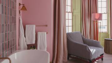 A bathroom with a white bathtub, striped armchair, and pink walls.