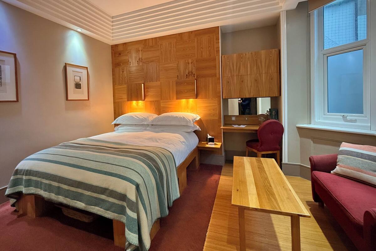 A hotel room with a bed, a desk, a chair, a sofa, and a large window.