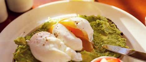 A breakfast plate with avocado toast, a poached egg, and a small bowl of fruit.