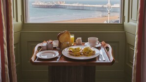 A breakfast tray with plates, cups, and toast on a table by a window with a view of a pier and beach. - Drakes of Brighton (Brighton)