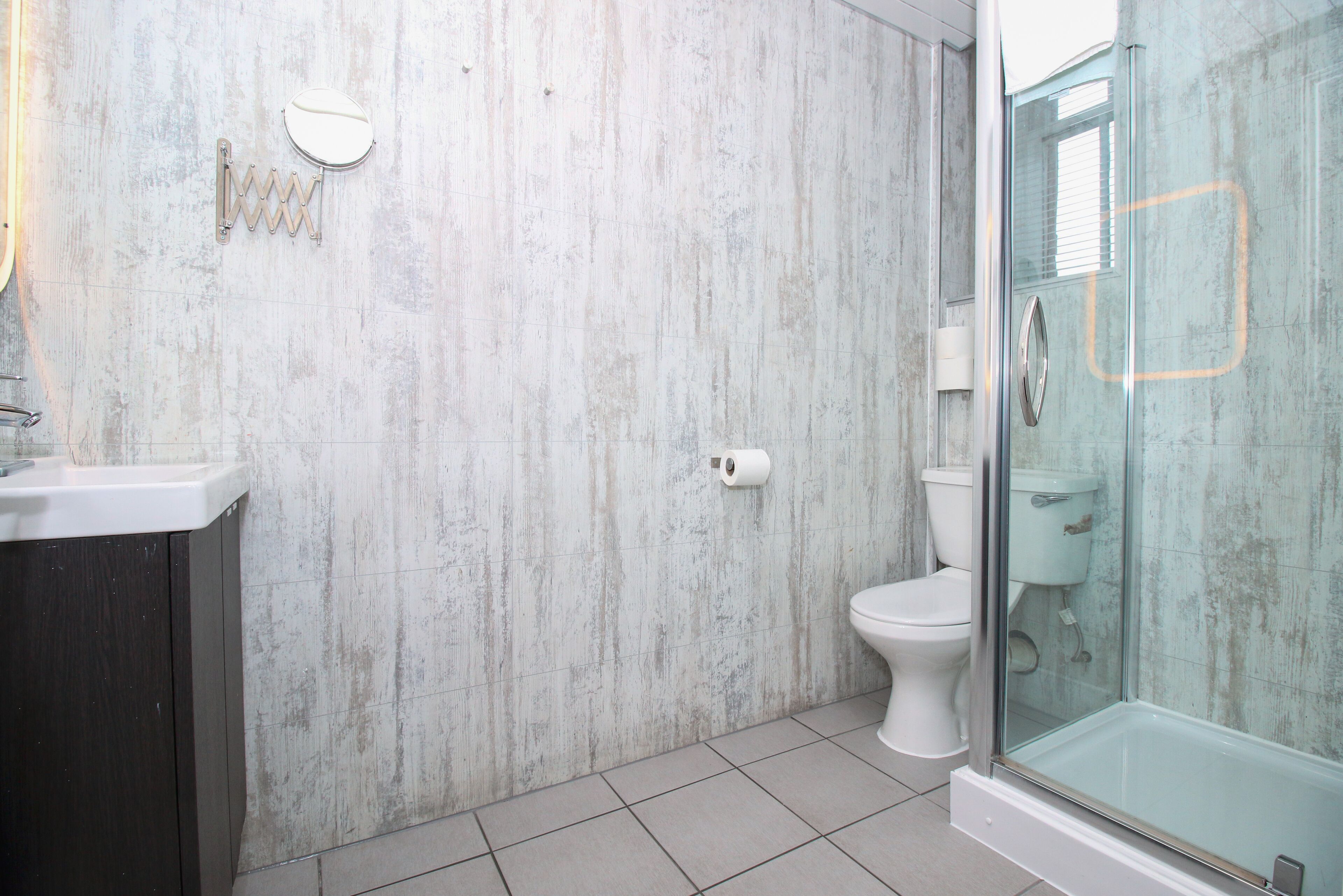 Une salle de bain avec un mur en marbre, des toilettes, une douche en verre et un meuble-lavabo de couleur foncée.