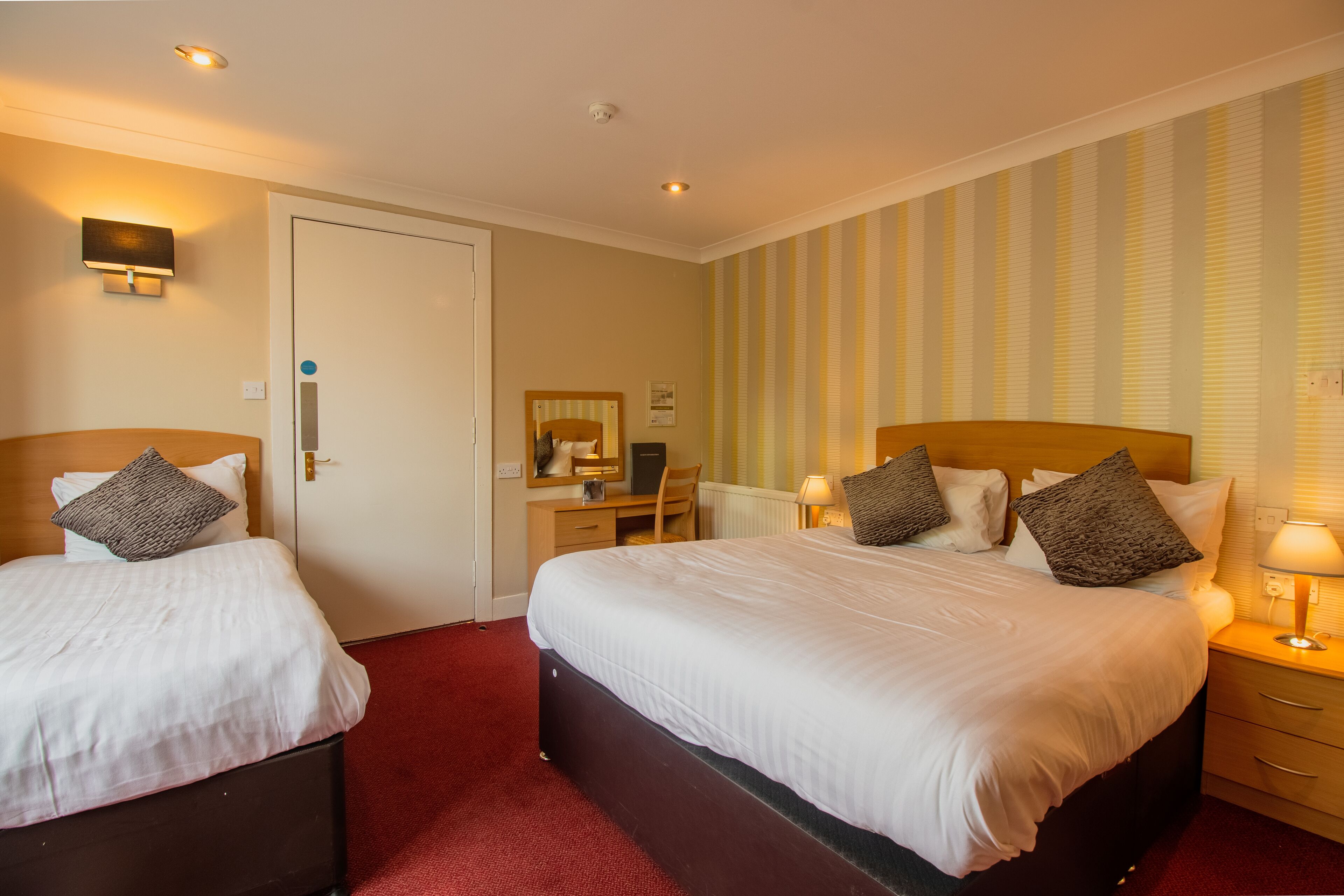 Ein Hotelzimmer mit zwei Betten, einem Schreibtisch, einem Stuhl, einem Spiegel und einer Heizung.