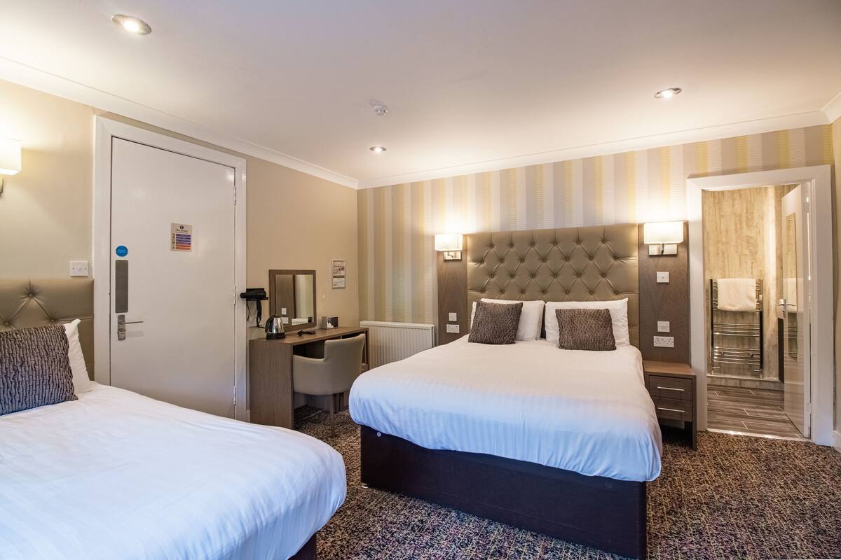 A hotel room with two beds, a desk, a chair, a large mirror, and a bathroom visible through an open door.