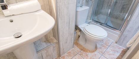 Un baño con lavamanos blanco, inodoro y cabina de ducha de vidrio.
