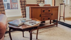 A room with a wooden cabinet, a table with books, a lamp, and a view of buildings through a window. - Newport Quay Bed and Breakfast (Newport)