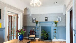 A room with a blue fireplace, a chandelier, and a dining area with a wooden table and chairs. - Boreland Lodge Hotel (Dunfermline)