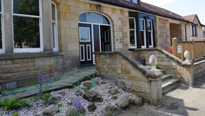A stone building with a black door, a small garden with rocks and purple flowers, and a wooden fence. - Boreland Lodge Hotel (Dunfermline)