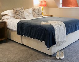 Una cama bien tendida con un edredón azul oscuro, almohadas blancas y una manta decorativa.