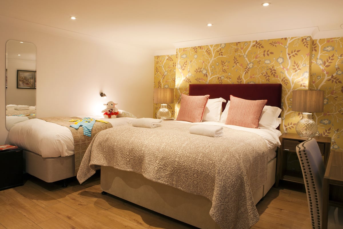 A double bed with a patterned bedspread, a nightstand with a lamp, and a mirror on the wall.