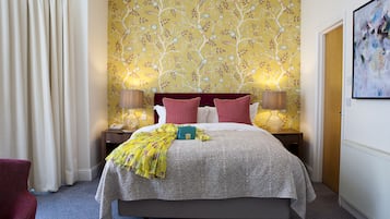 Una cama bien tendida con un edredón estampado, dos lámparas de noche y un fondo de papel tapiz floral.