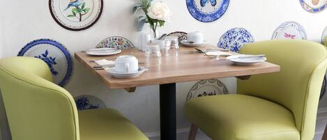 Una mesa de comedor con platos blancos, tazas y un florero con flores, rodeada por dos sillas amarillas.