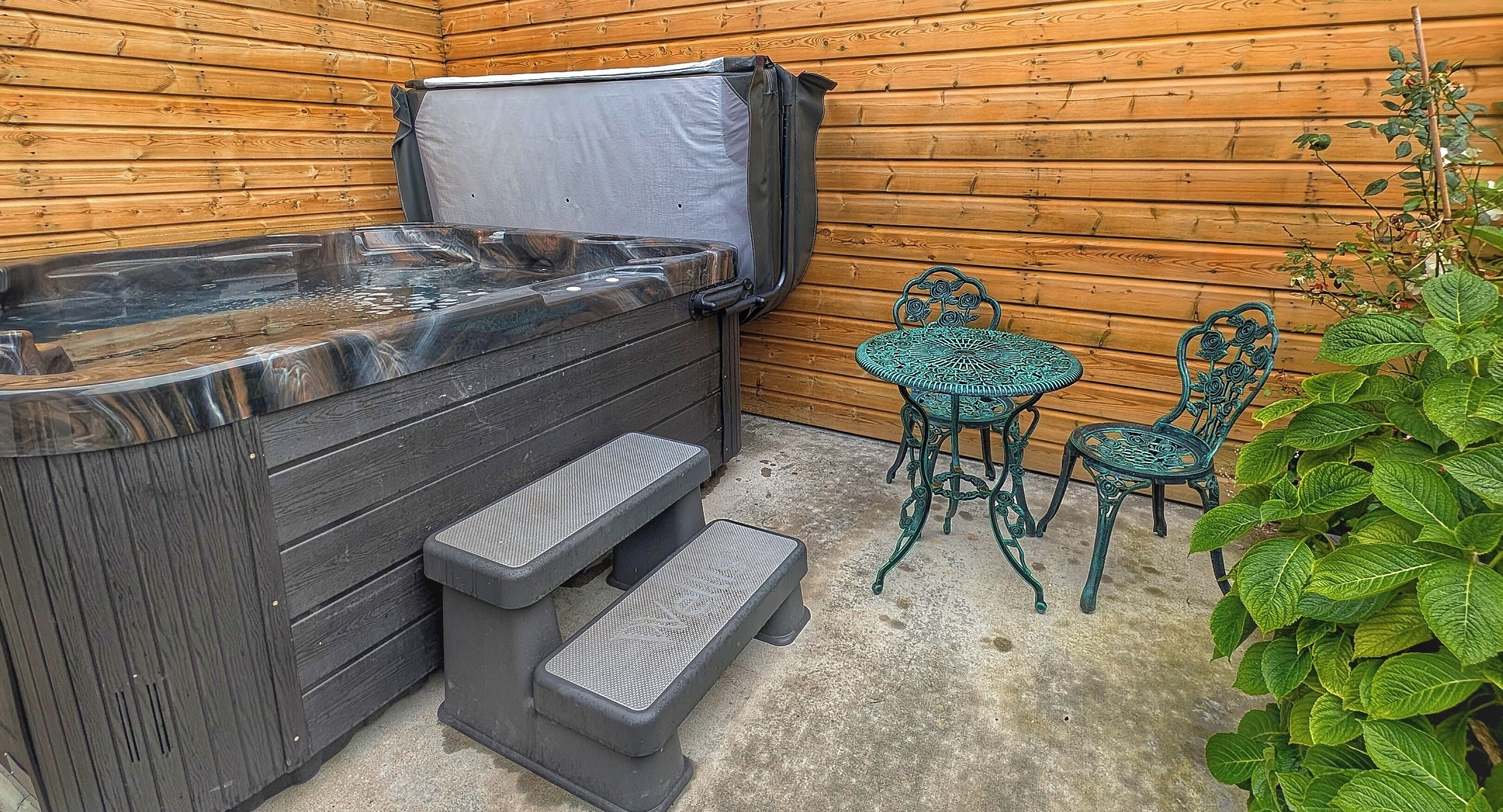 Un bain à remous avec des marches, deux chaises en métal et une petite table, le tout installé dans un espace extérieur en bois.