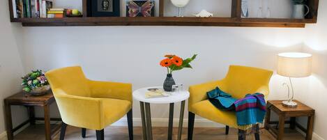 A room with two yellow chairs, a small white table with a vase of flowers, and a lamp on a wooden side table.