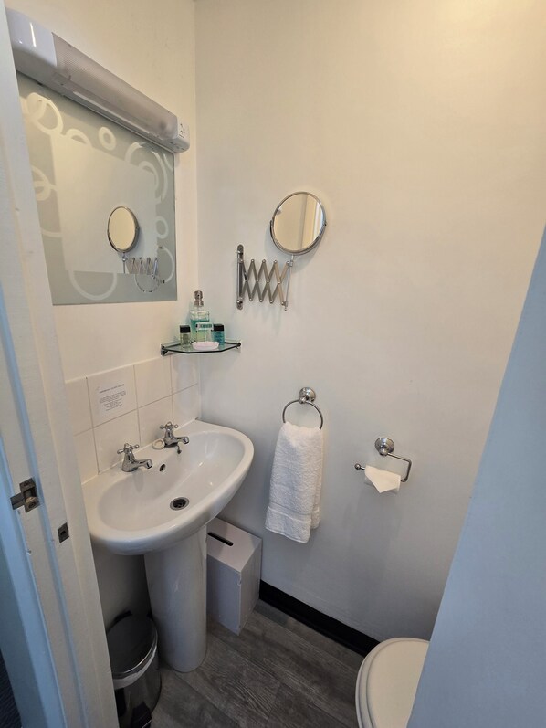 Un baño con lavamanos, espejo, toallero y retrete.