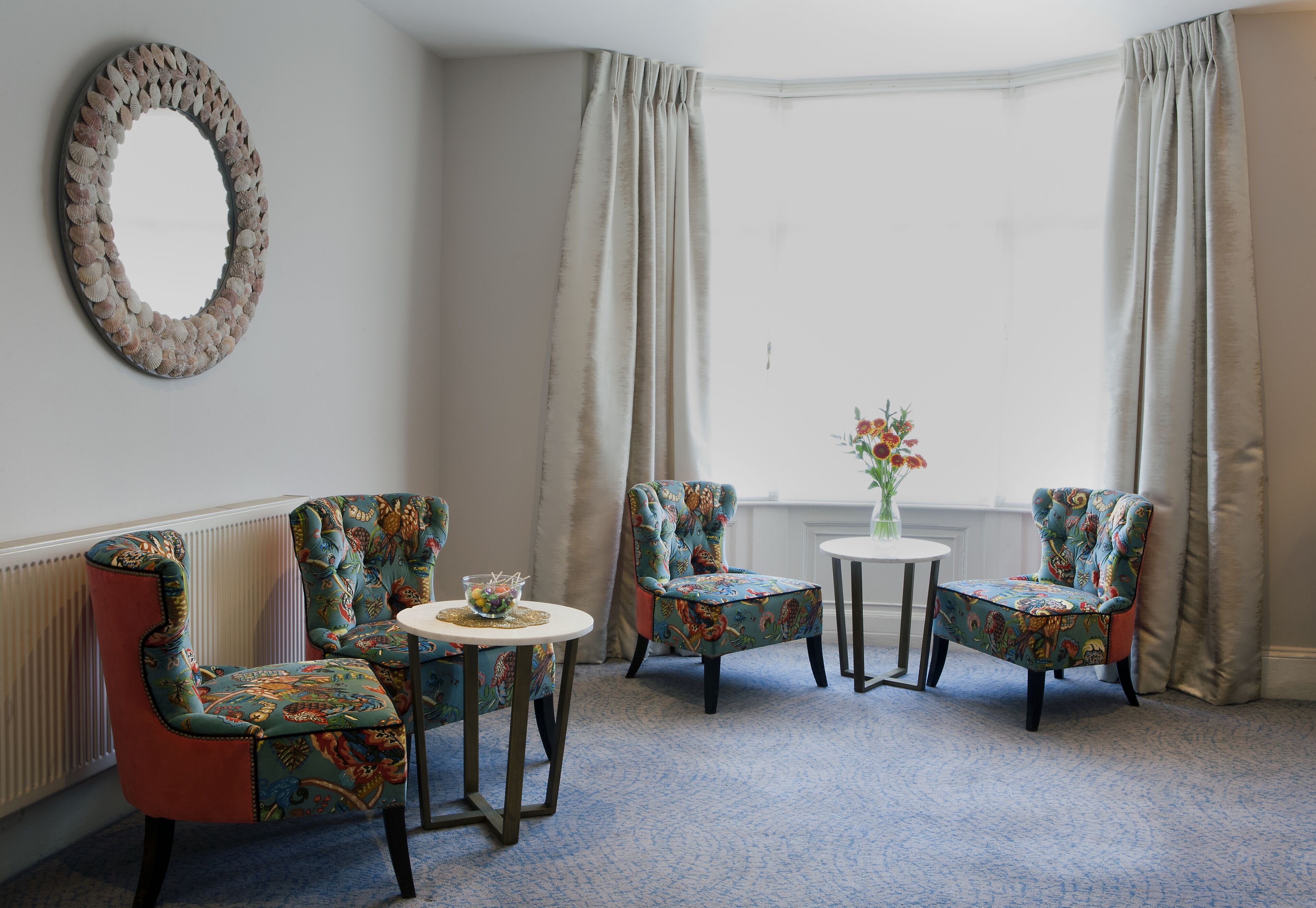 A room with two armchairs, a small table, a mirror, and a window with curtains.