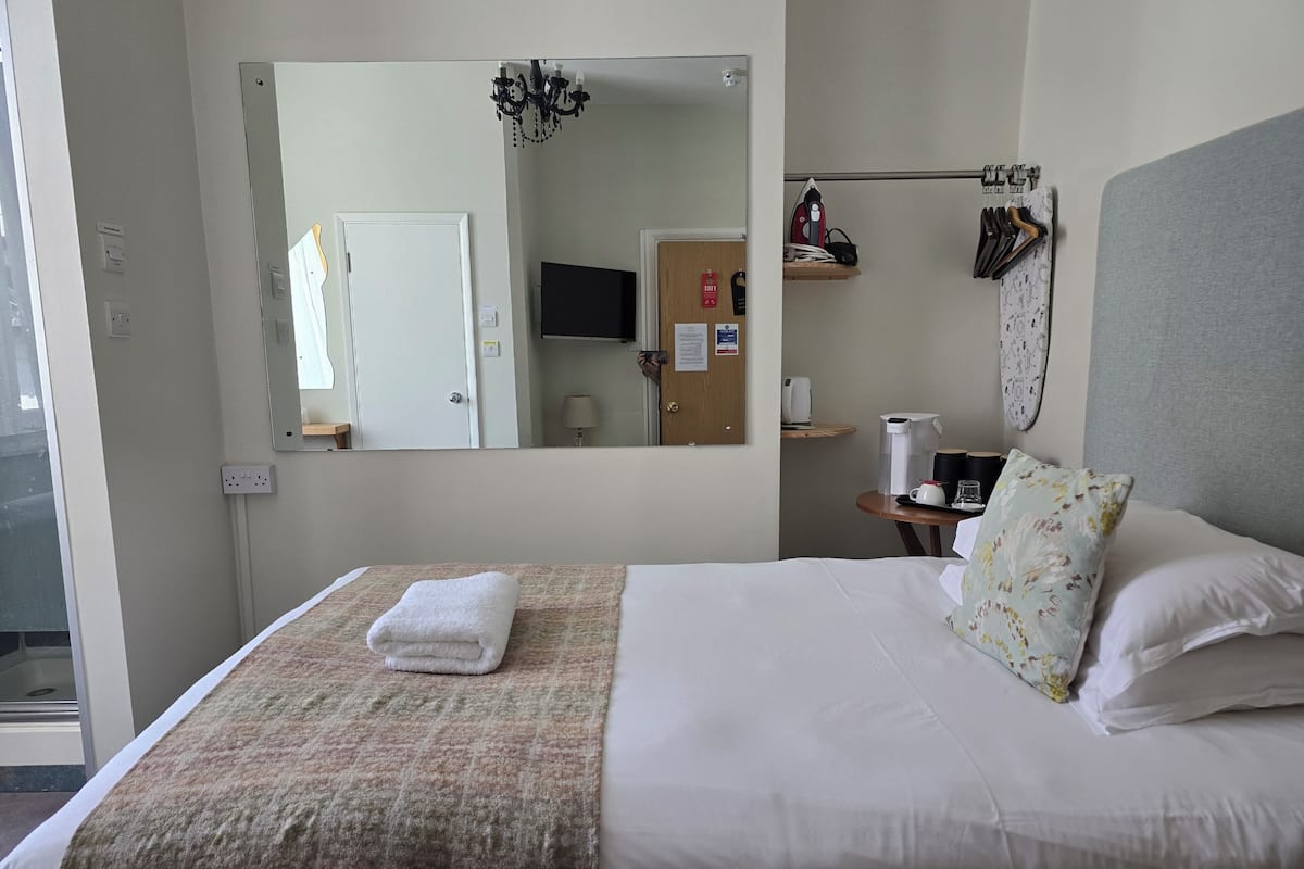 A hotel room with a bed, a mirror, a television, a coffee maker, and a shelf with items.