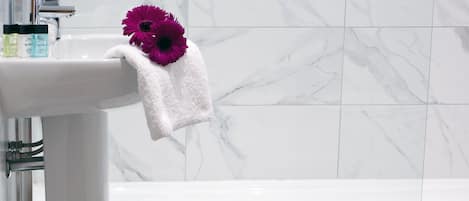 Un baño con un lavamanos blanco, una bañera blanca y una pared de mármol.