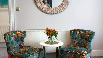 Una habitación con dos sillones estampados, una mesita redonda con un florero y un espejo decorativo en la pared.