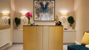 A reception area with a curved wooden desk, two wall-mounted lamps, a framed artwork, and potted plants. - Sea Spray (Brighton)
