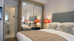 A hotel room with a large bed, a bedside table with lamps, a mirror, and a sliding door leading to a bathroom. - Sea Spray (Brighton)