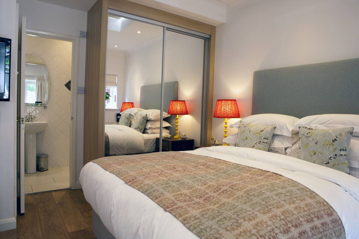 A hotel room with a large bed, a bedside table with lamps, a mirror, and a sliding door leading to a bathroom.