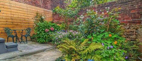 Pared de tijolos com um banco de madeira e degraus que levam a um jardim com diversas plantas e flores.